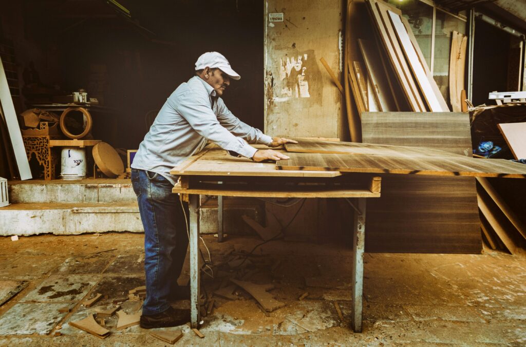Carpenter focuses on woodworking project inside a busy workshop, surrounded by materials.